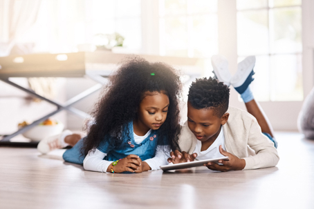 Two kids laying on the floor playing on a tablet